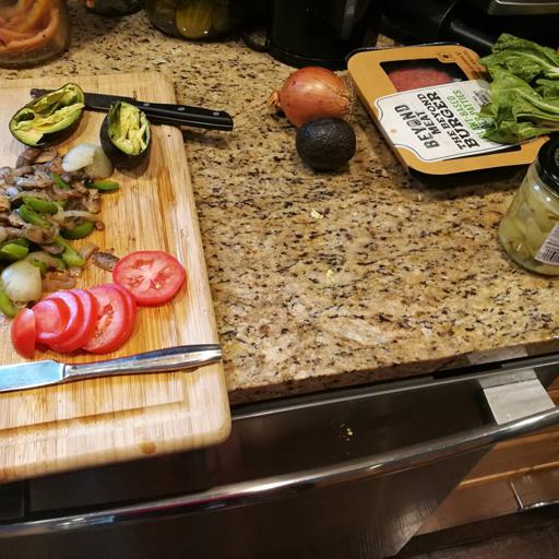 Homemade Beyond Meat Burger Vegan and Plant Based on Whole Wheat Bun and tons of toppings in jars: fresh tomatoes plus cooked onions, green pepper, and mushrooms